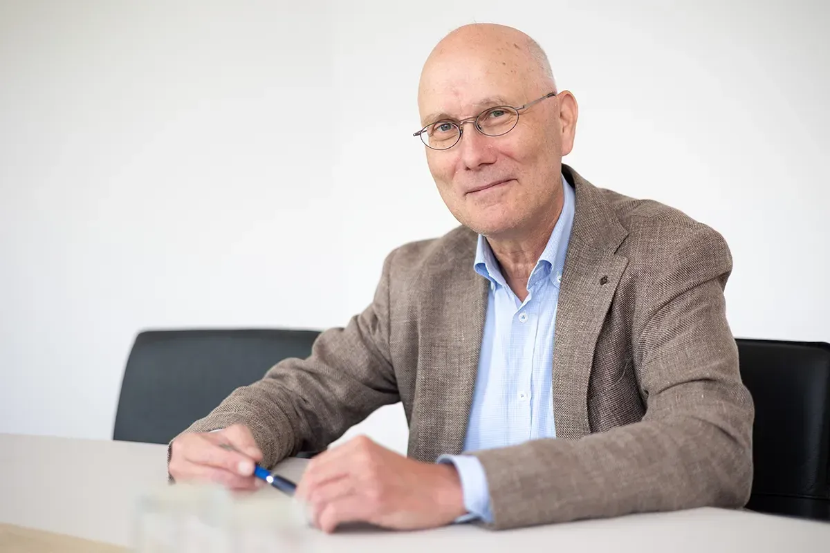 Ein kahlköpfiger Mann sitzt mit einem Stift in der Hand an einem Tisch.