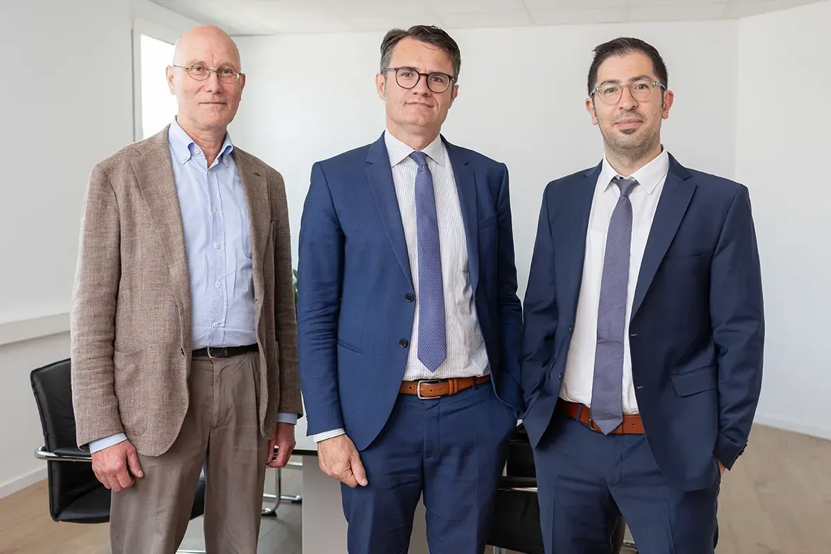Drei Männer in Anzug und Krawatte posieren für ein Foto.
