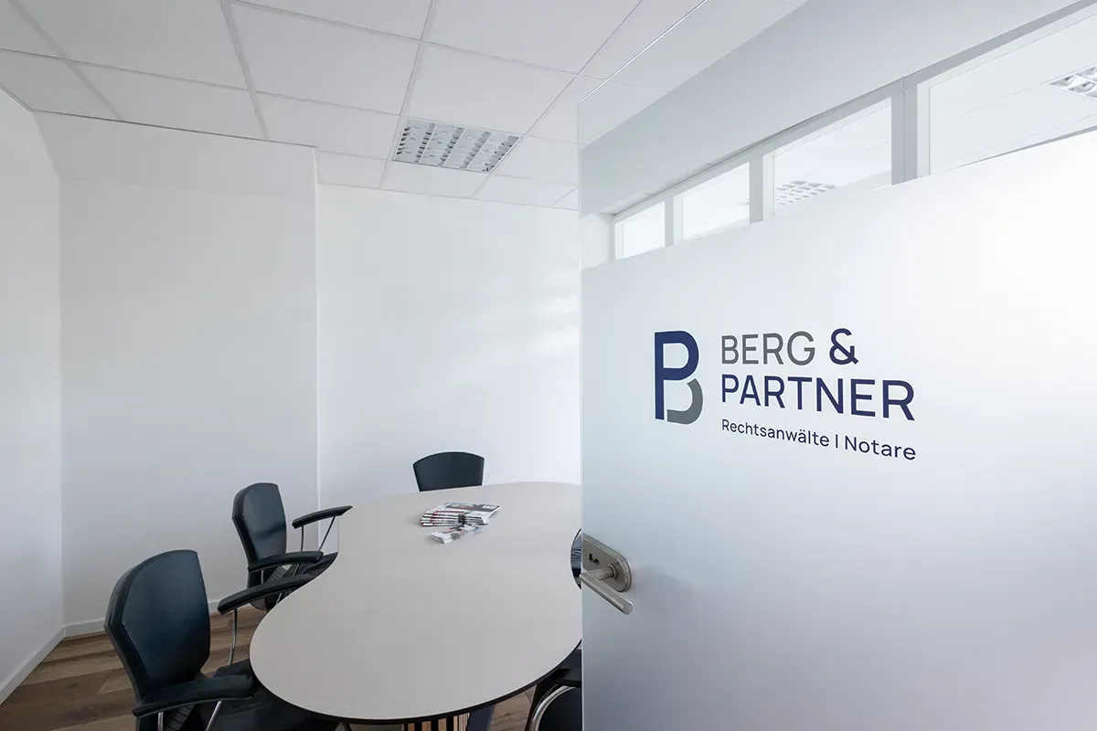 Ein Konferenzraum mit einem Tisch und Stühlen und einer Glastür mit der Aufschrift „Berg & Partner“.