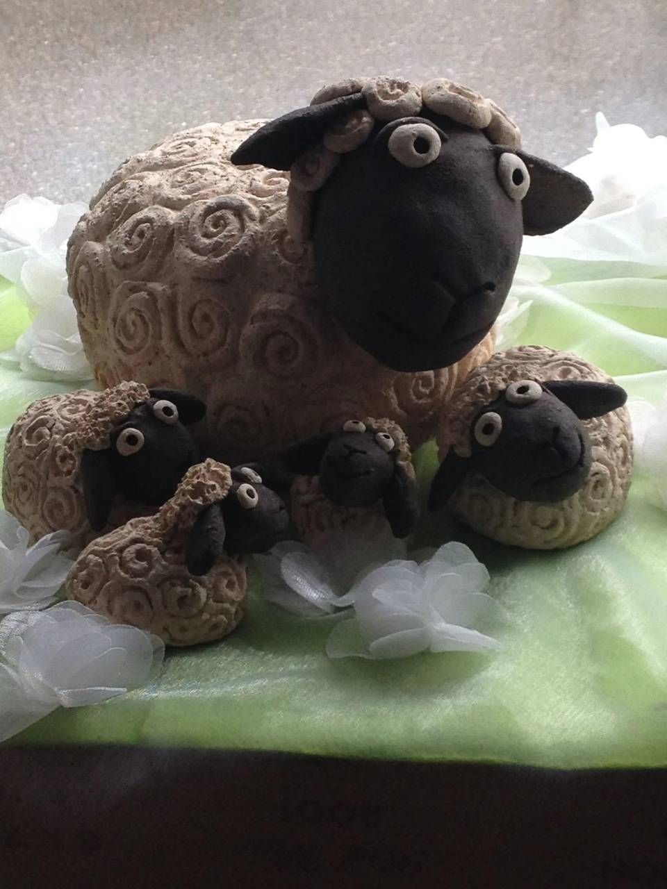 Zwei Wollschaffiguren auf grünem Stoff, eine grosse und zwei kleine, mit gekräuselter Wolle und runden Augen