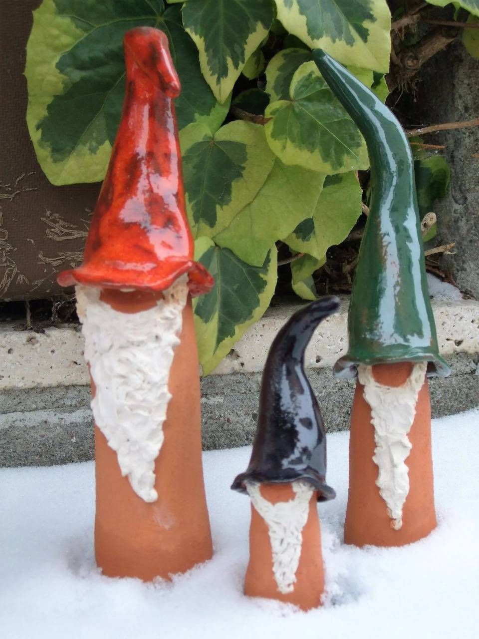 Drei bemalte Gnomefiguren mit roten, schwarzen und grünen Hüten vor grünem Hintergrund