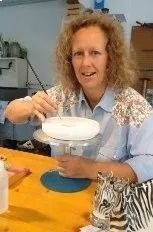 Eine Frau sitzt an einem Tisch und hält eine weisse Schüssel; im Vordergrund ist ein Zebra-Plüschtier zu sehen.