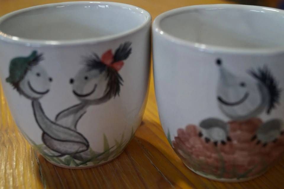 Zwei bemalte Keramikbecher mit lächelnden Figuren auf einem Holztisch