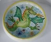 Illustration eines grünen Drachen auf einem runden Teller mit blauen Blumen und gelbem Rand