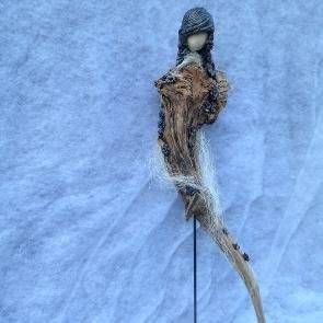Kleine, handgefertigte Figur mit dunkler Kapuze, braunem Körper und langem, dünnem Schwanz vor blauem Stoffhintergrund