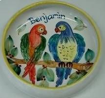 Zwei bunte Papageien auf einem Ast in einem runden Teller, darüber steht „Benjamin“.
