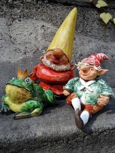 Drei kleine Gartenzwerge auf Steinstufen, darunter ein grüner Froschzwerg und eine sitzende Figur in Rot und Grün.