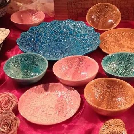 Bunte, dekorative Keramikschüsseln und -teller sind auf einem leuchtend rosa Tuch arrangiert.