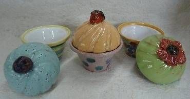 Drei farbenfrohe, cupcake-förmige Dessertschalen mit Deckeln auf einer weissen Oberfläche