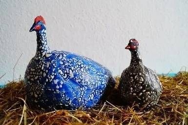 Zwei dekorative, gesprenkelte Vögel, einer blau und einer schwarz, ruhen auf Stroh.