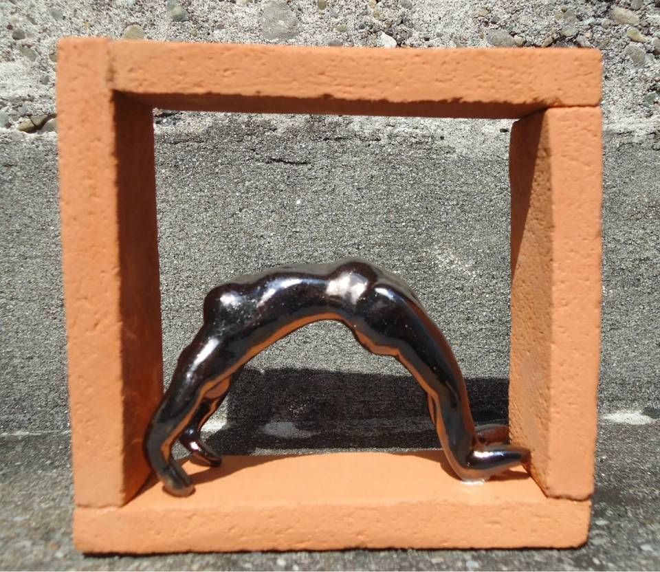 Schwarze abstrakte Metallskulptur, die sich innerhalb eines orangefarbenen quadratischen Rahmens auf einer Betonfläche wölbt.
