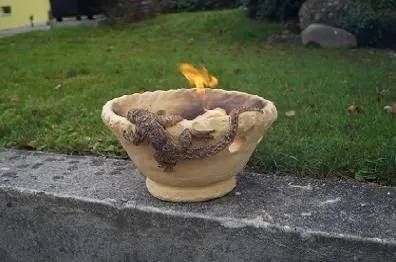 Ein kleines Feuer brennt im Freien in einer Steinschale auf dem Bordstein neben einer Rasenfläche.