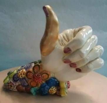 Keramische Daumen-hoch-Figur mit floralem Sockel und bemalten Fingernägeln auf hellem Hintergrund