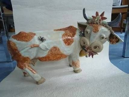 Weisse und orangefarbene Kuhfigur mit Hörnern und Blumenverzierungen auf blauem Boden