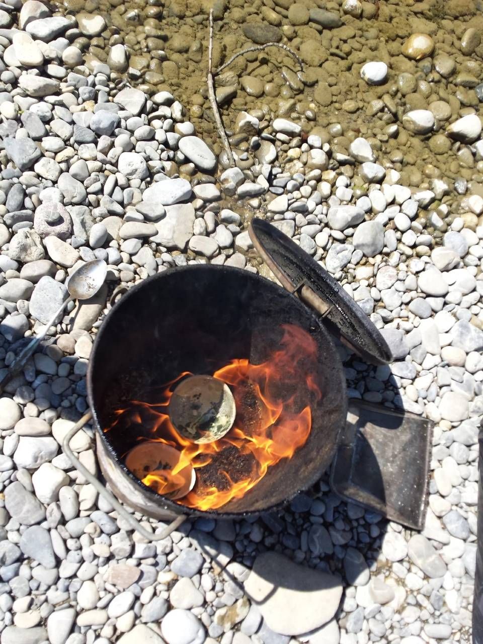 Draufsicht auf eine kleine, brennende Metallfeuerstelle auf weissem Kies, umgeben von Steinen.