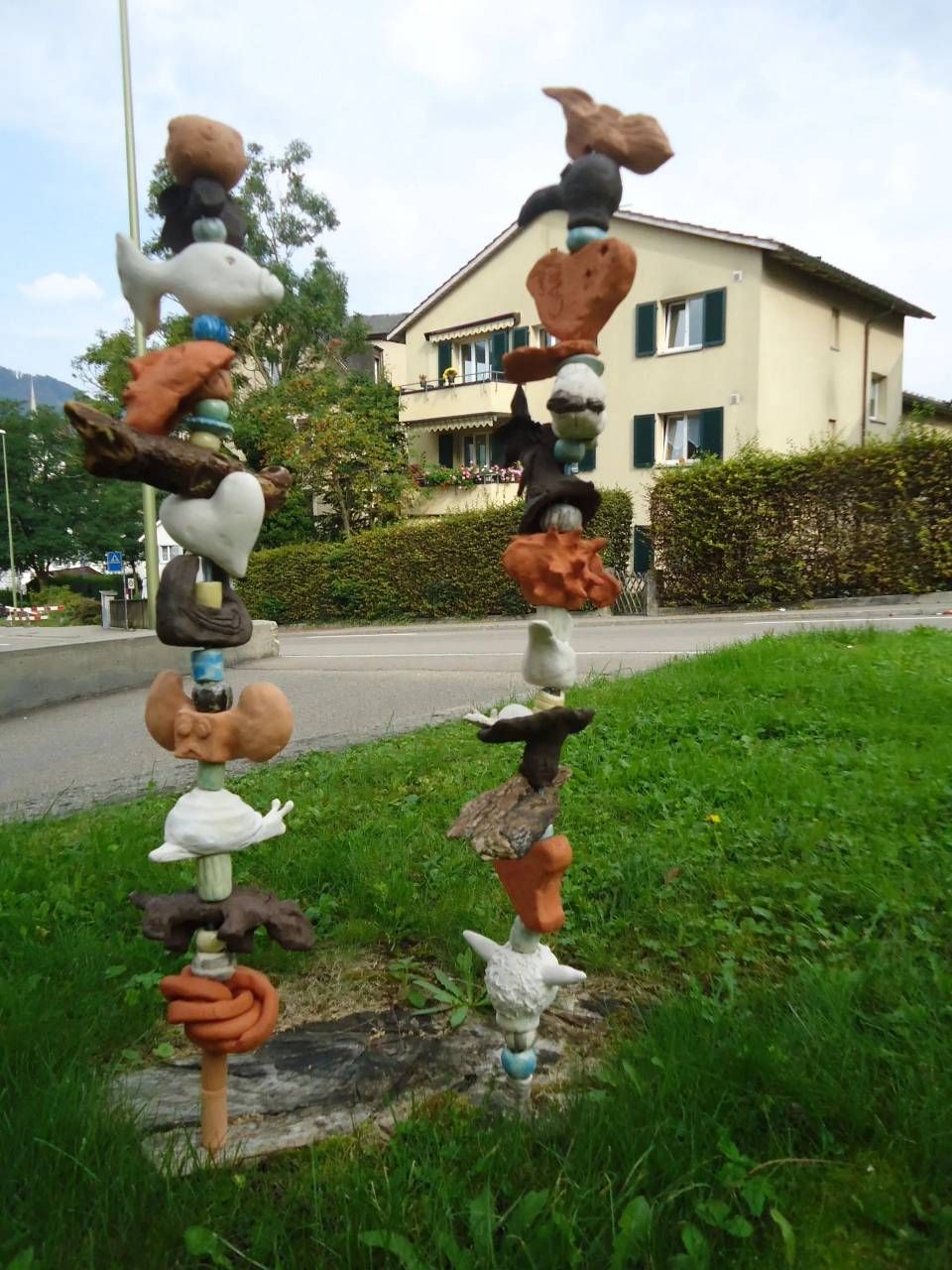 Bunte, gestapelte Gartenskulpturen neben einer Rasenfläche und einem Haus in einem Wohngarten