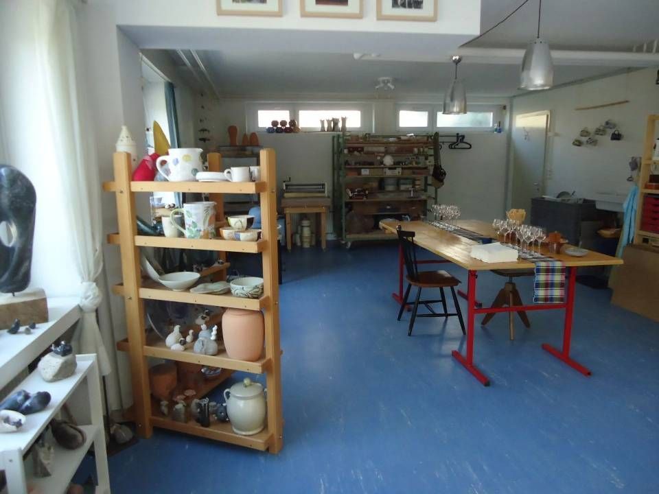 Helles Töpferatelier mit Regalen voller Keramik, Arbeitstischen und blauem Bodenbelag