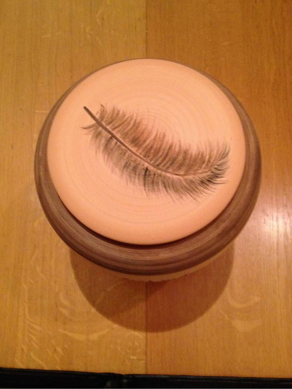 Federförmige Wimpernmarkierung, eingeprägt in einem runden, rosafarbenen Kompaktpuder auf einem Holztisch