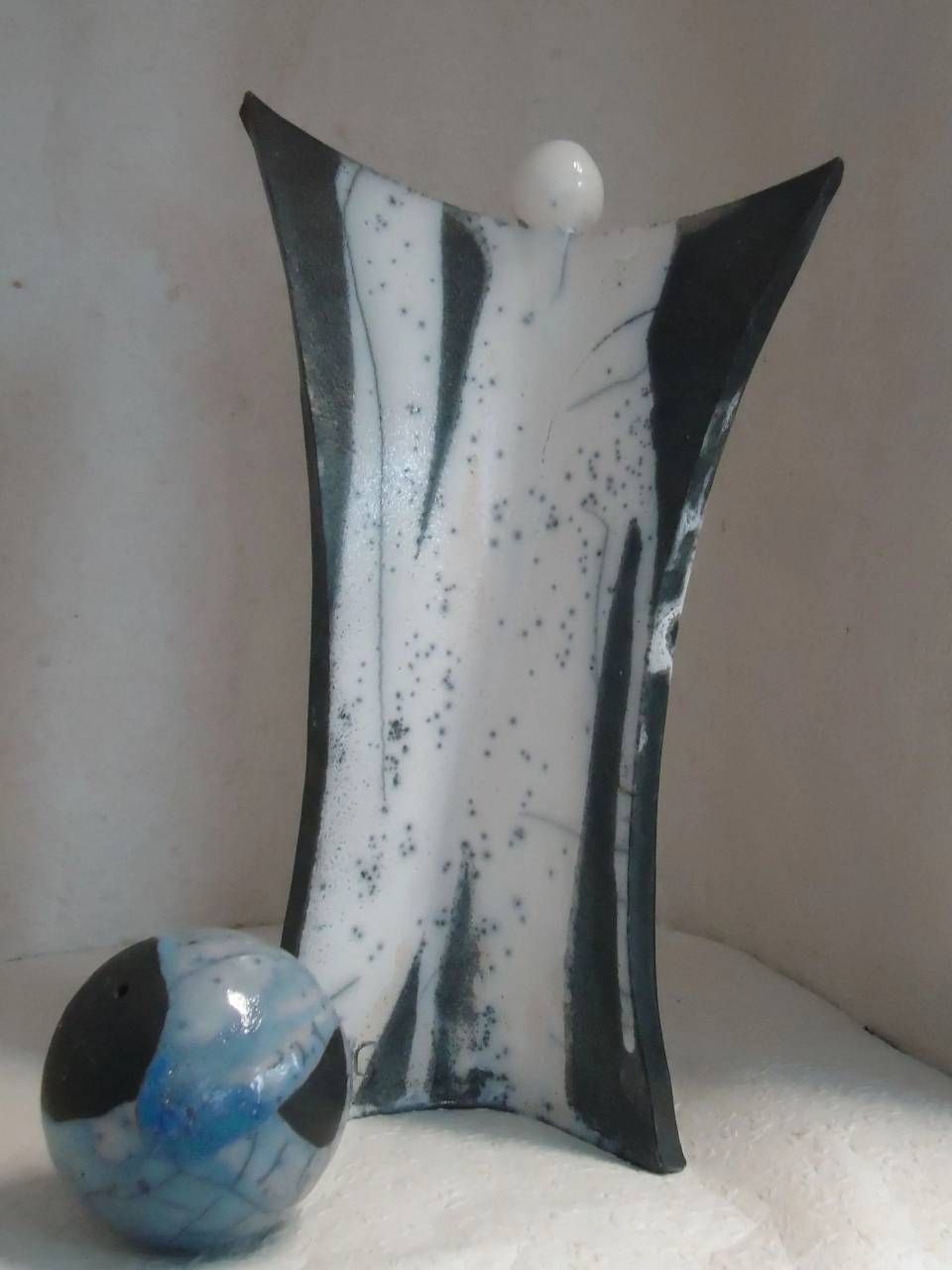 Abstrakte schwarz-weisse Keramikskulptur mit einer blauschwarzen Kugel auf hellem Untergrund.