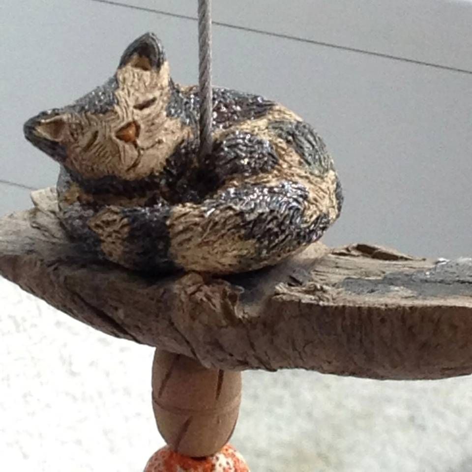 Eine kleine Katzenfigur, die um ein hängendes Holzregal gewickelt ist, durch das eine Schnur verläuft.