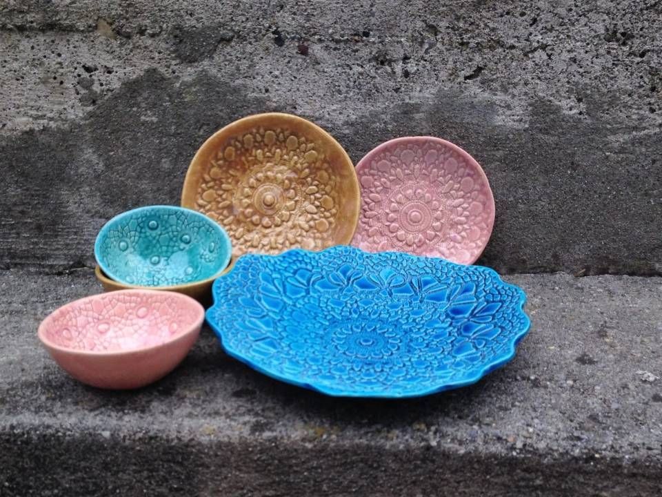 Bunte Dekoteller und -schalen sind auf einer Steinfläche vor einer grauen Wand arrangiert.