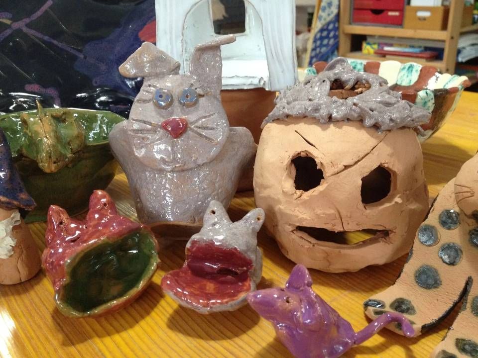 Handgefertigte Keramiktassen und Tierfiguren auf einem Tisch, darunter eine Tasse mit Katzenkopf und bunte Becher.