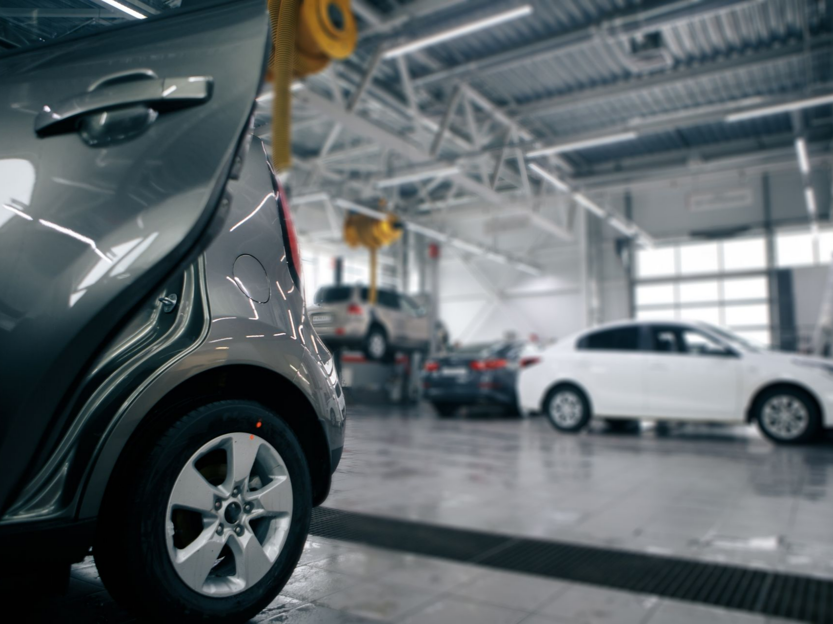 Voiture grise au premier plan, portière ouverte, à l'intérieur d'un garage, autres voitures floues en arrière-plan.