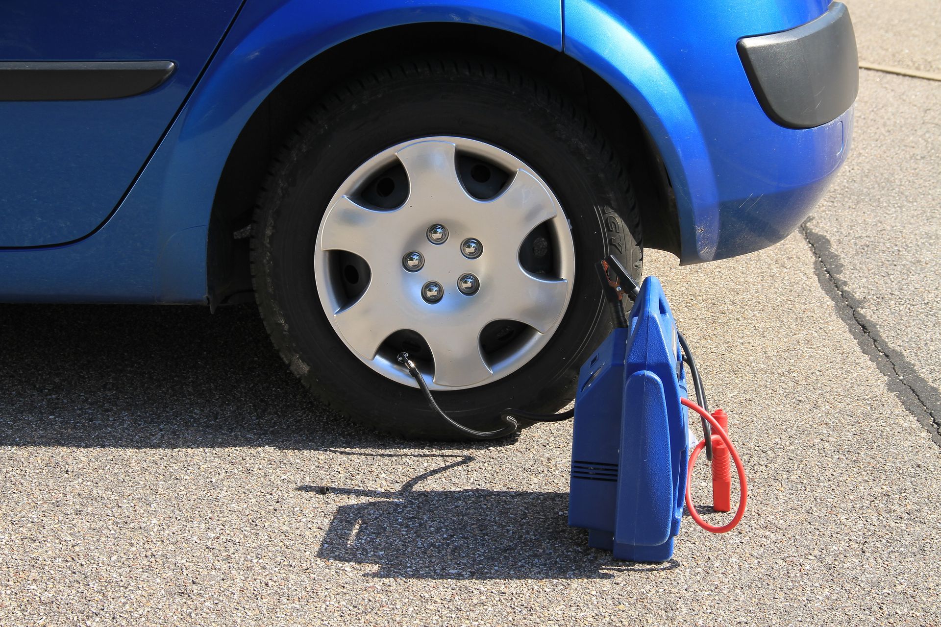 Un pneu de voiture bleu est gonflé sur l'asphalte à l'aide d'un compresseur d'air portable bleu.