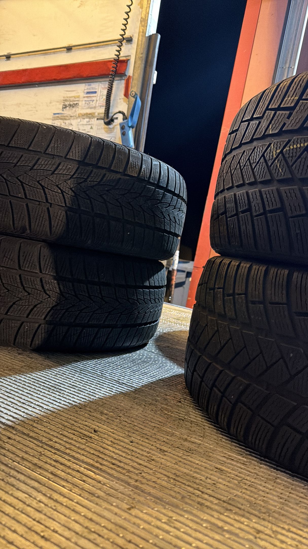 Des pneus en caoutchouc noir, aux sculptures détaillées, sont empilés sur une surface texturée dans un atelier.
