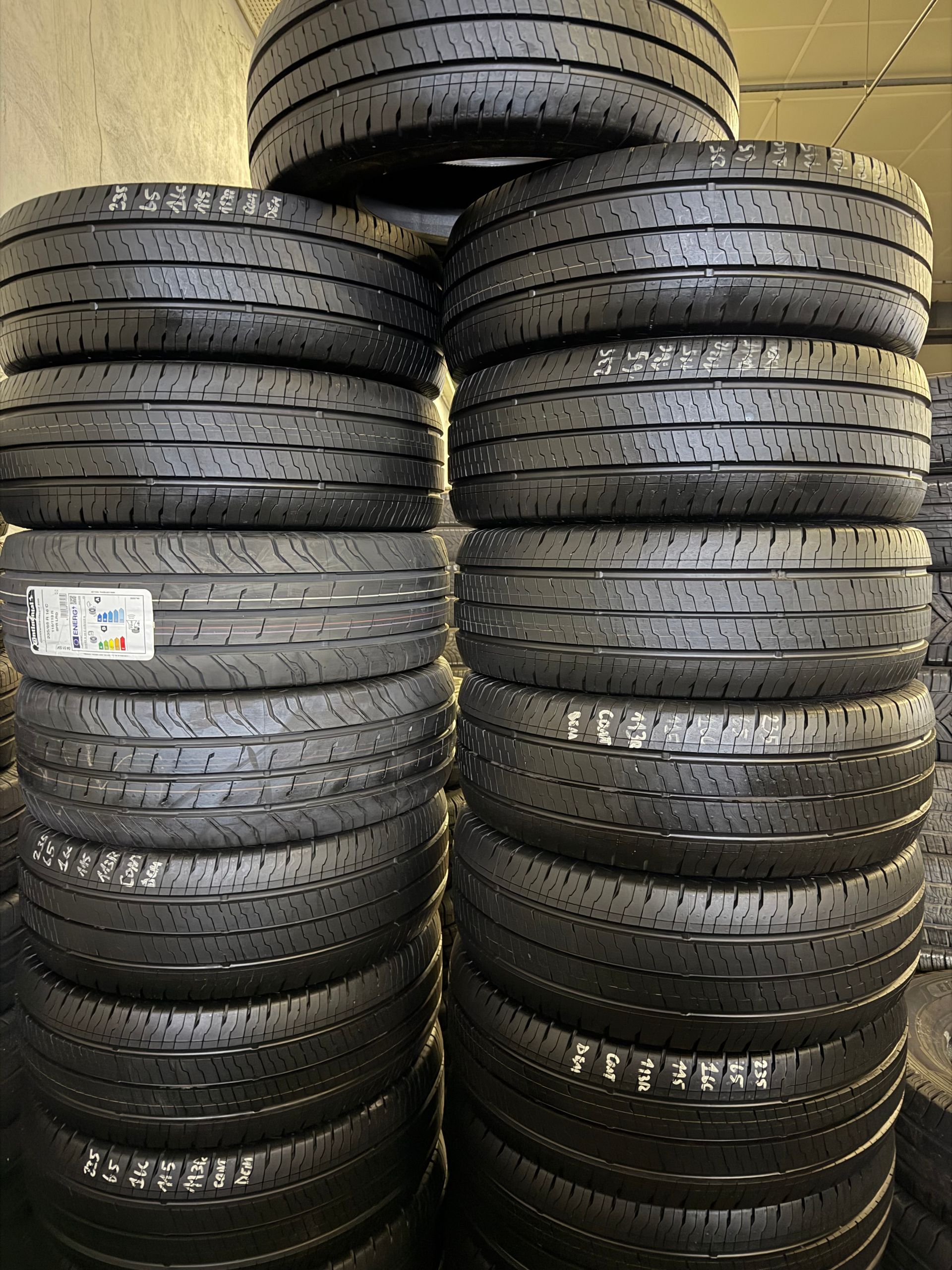 Deux hautes piles de pneus noirs de véhicules, côte à côte, dans un entrepôt.