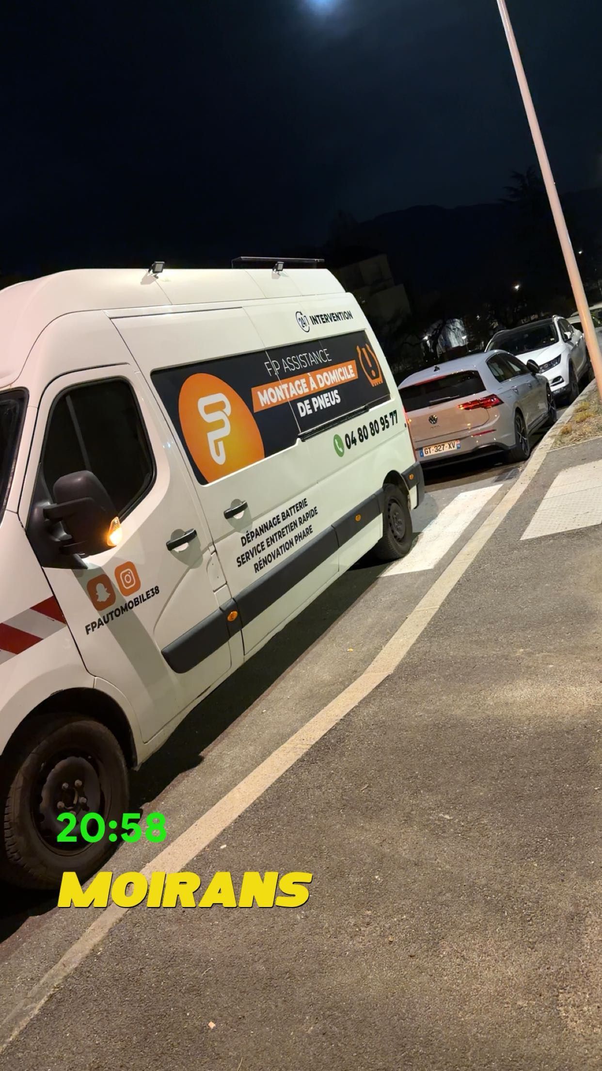 Une camionnette de livraison blanche garée en bord de route la nuit.