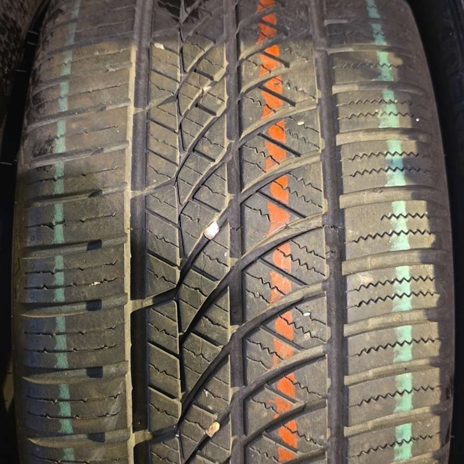 Gros plan sur la bande de roulement d'un pneu noir neuf présentant des bandes de guidage verticales orange et vertes bien distinctes.