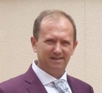 Hombre con traje morado y corbata estampada, sonriendo.