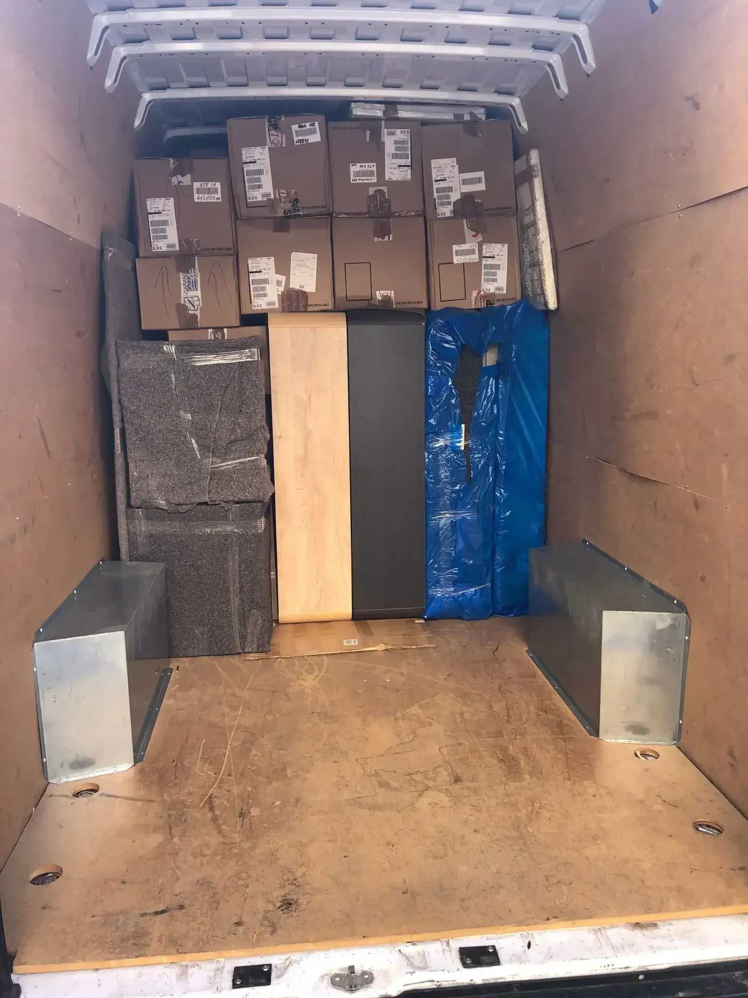 Interior de una furgoneta de carga repleta de cajas de cartón, paneles de madera y material protector.