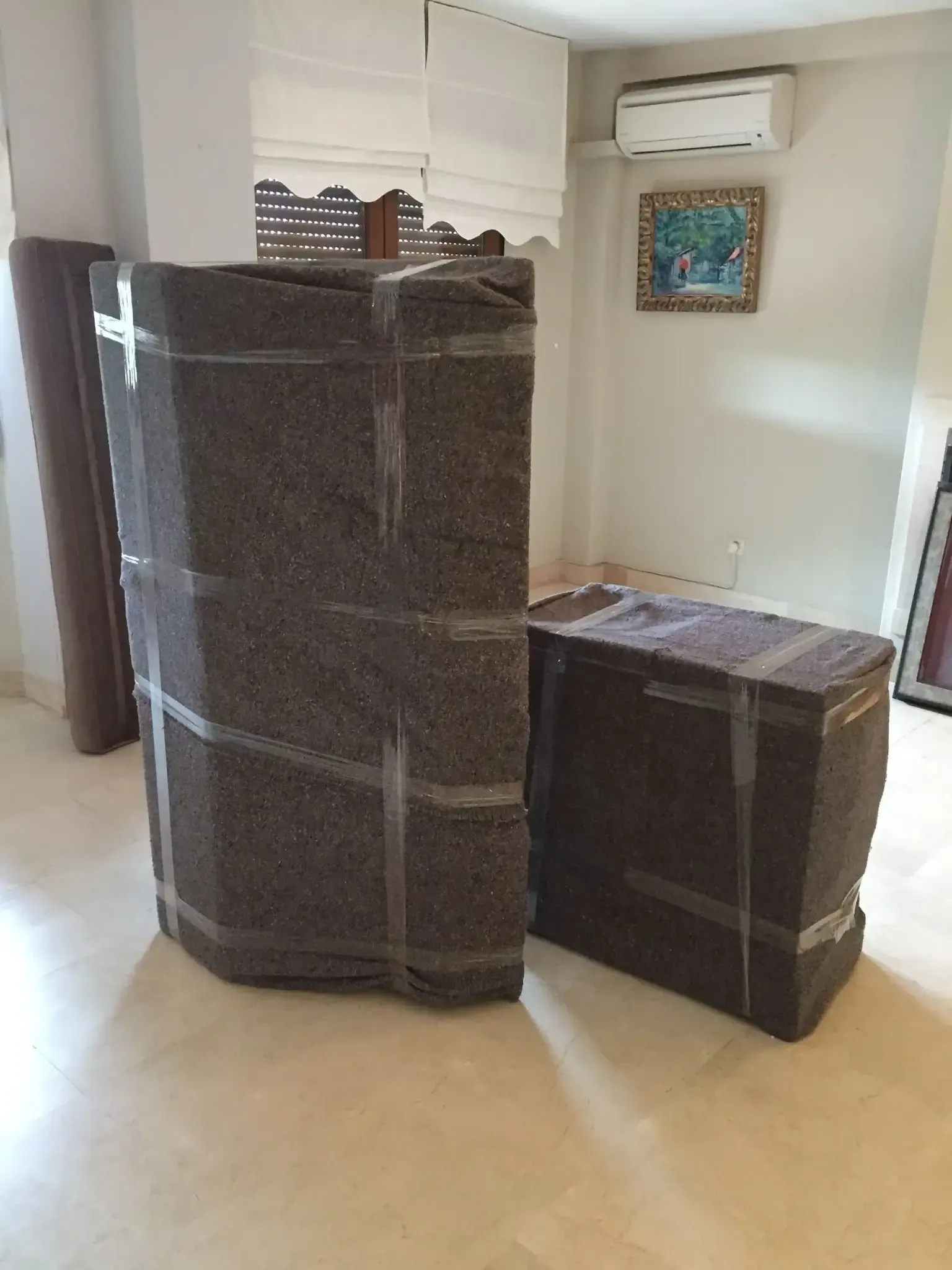 Dos muebles envueltos en espuma y cinta adhesiva, en el interior. Una alfombra enrollada está junto a ellos.