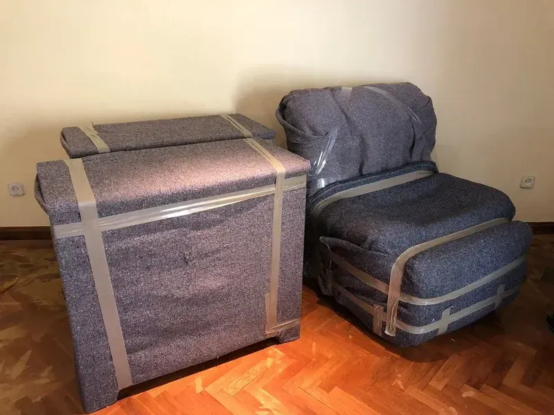 Dos muebles tapizados envueltos en acolchado protector y cinta adhesiva.