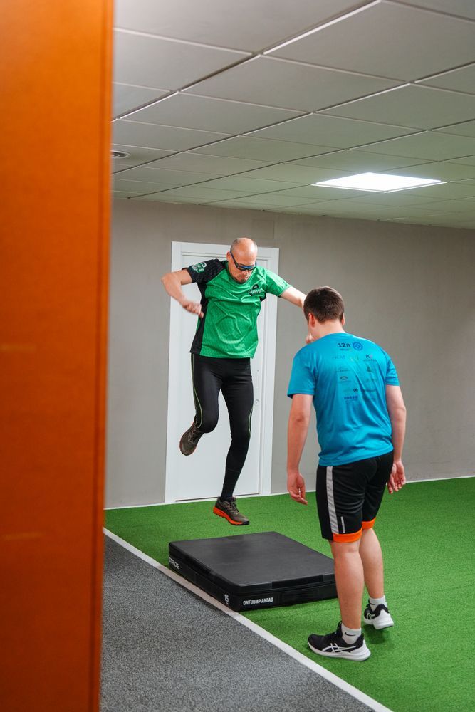 A man is jumping over a mat while another man watches.
