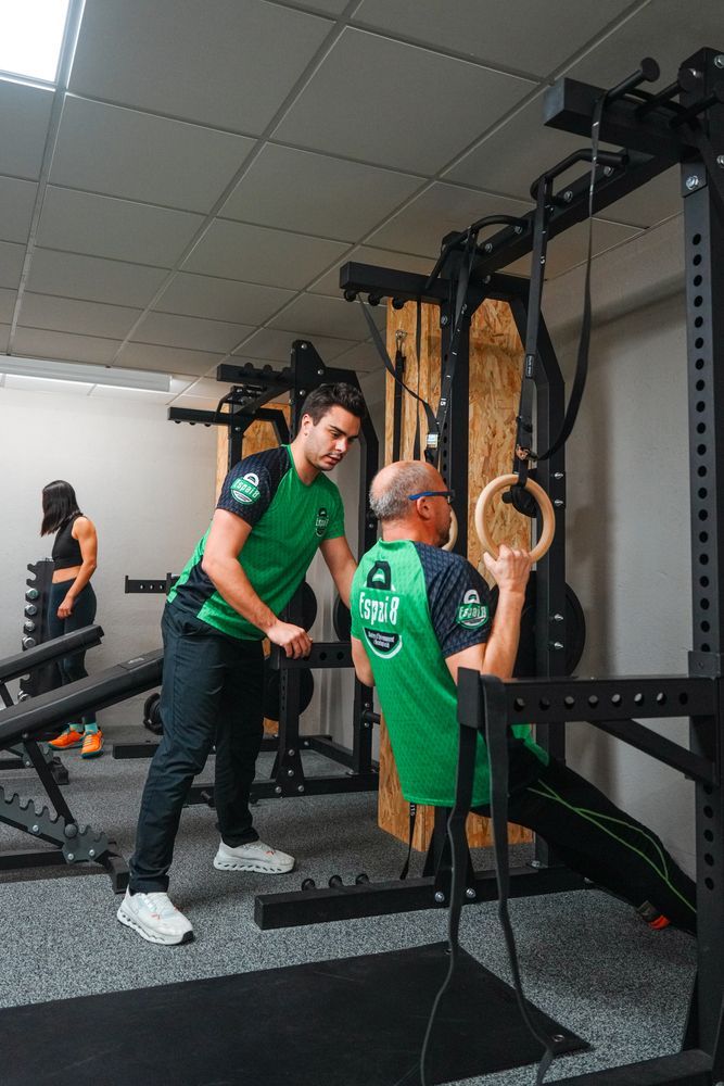 A man is helping another man do exercises in a gym.