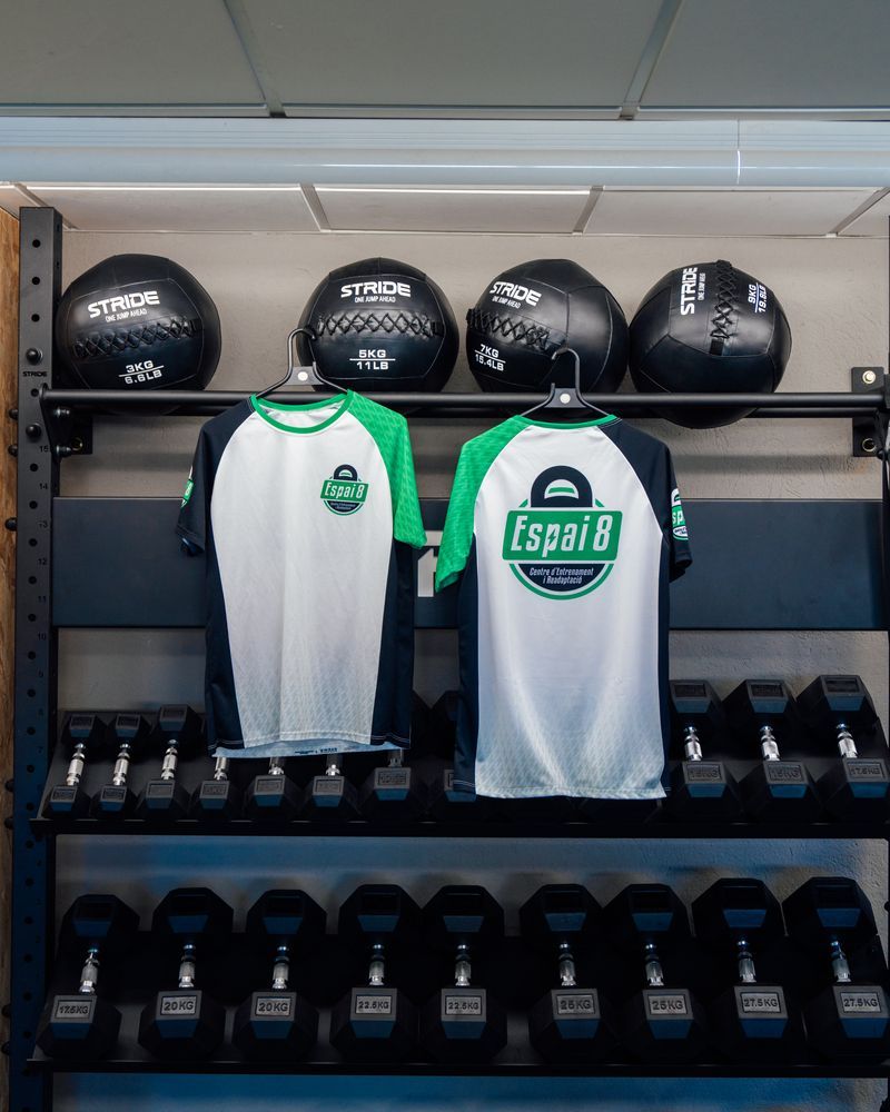 Dos camisetas están colgadas en un perchero en un gimnasio.