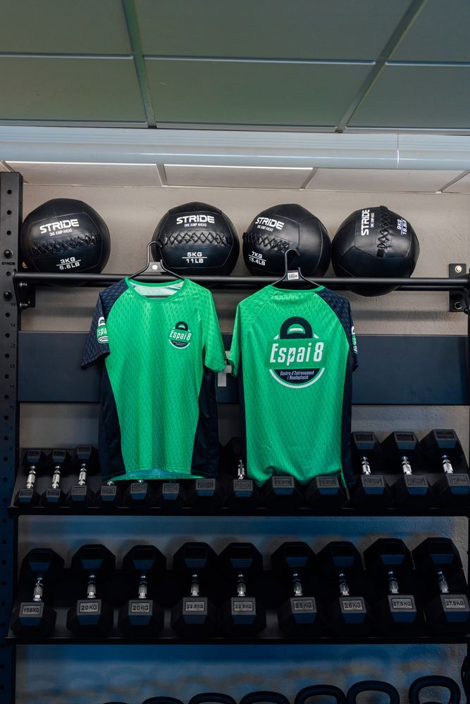 Dos camisetas verdes están colgadas en un perchero en un gimnasio.