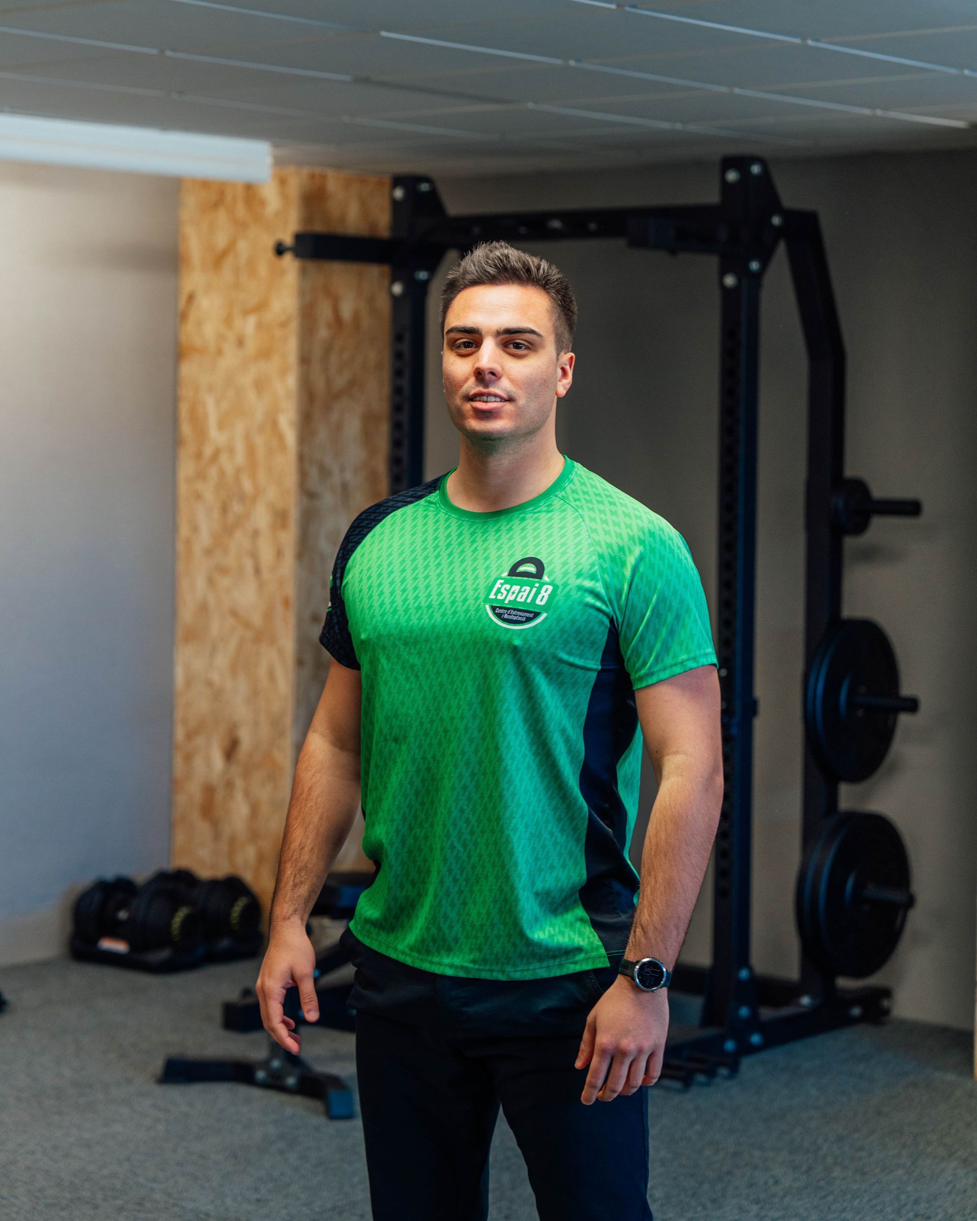 Un hombre con una camisa verde está de pie en un gimnasio.