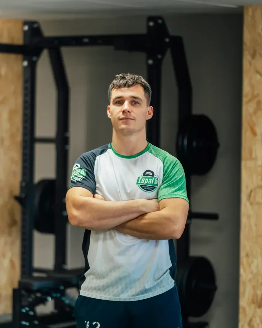 Un hombre está de pie en un gimnasio con los brazos cruzados.