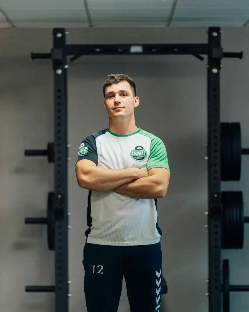 Un hombre está de pie en un gimnasio con los brazos cruzados.