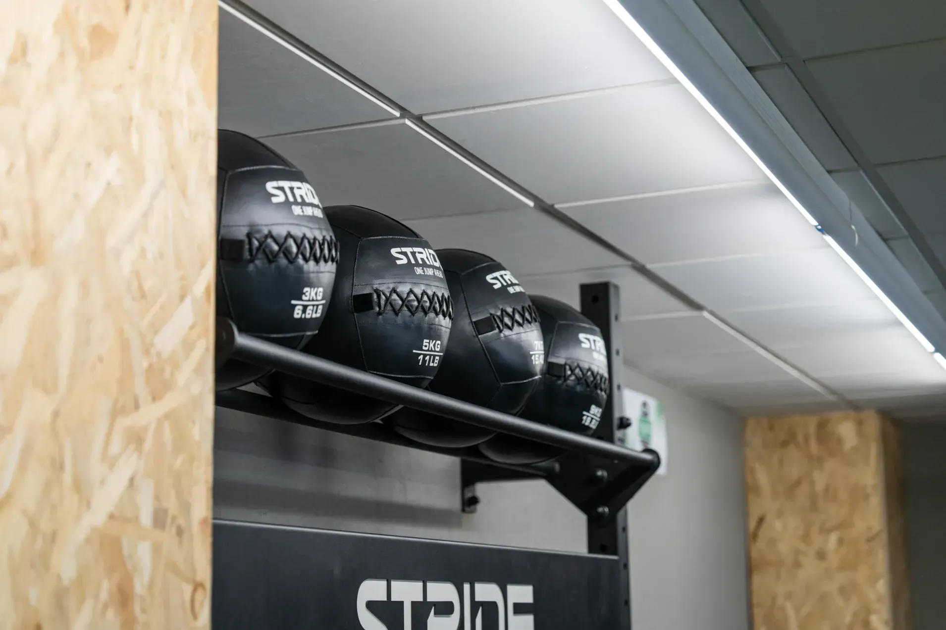 Una fila de balones medicinales negros cuelgan de un estante en un gimnasio.