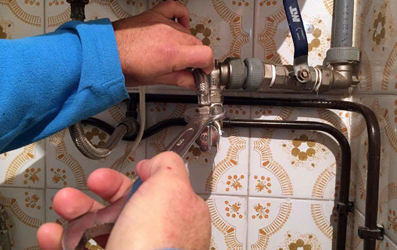 Una persona está arreglando una tubería con una válvula de bola azul.