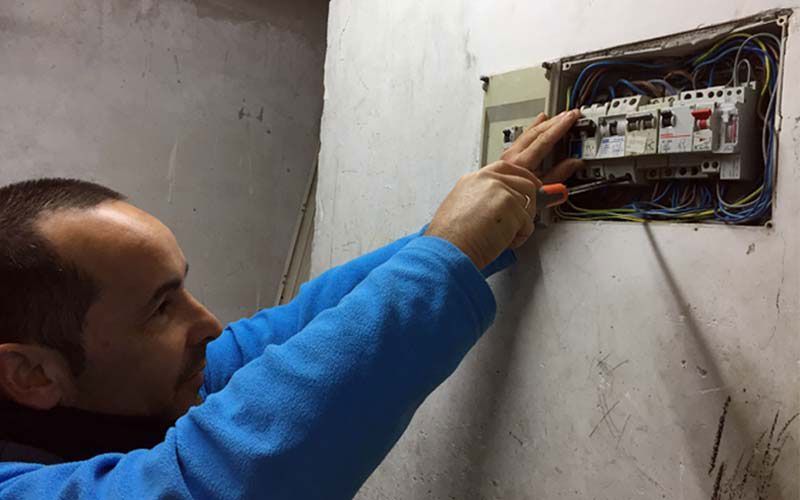 Un hombre con un suéter azul está trabajando en una caja eléctrica.