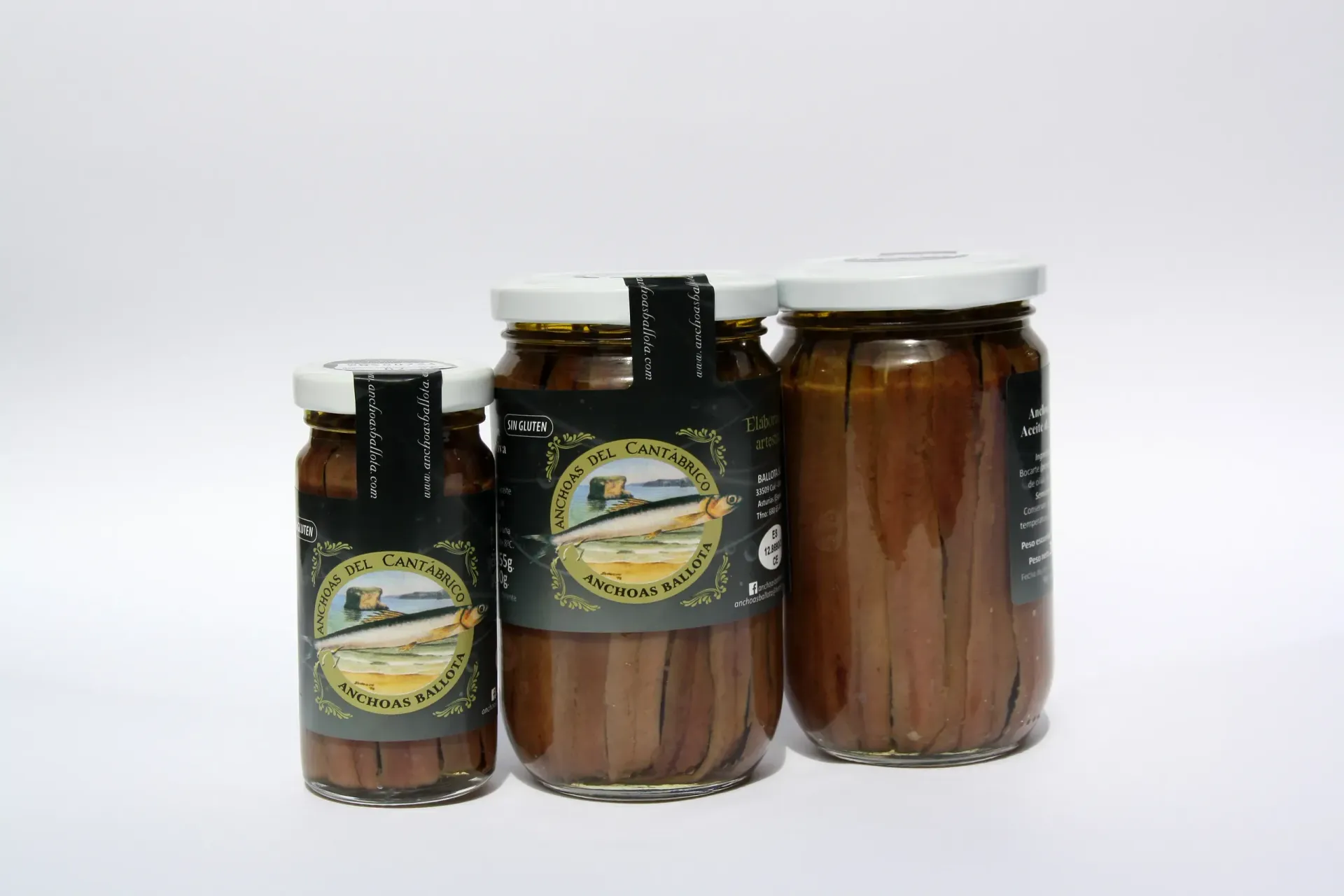 Tres frascos de anchoas están uno al lado del otro sobre una superficie blanca.