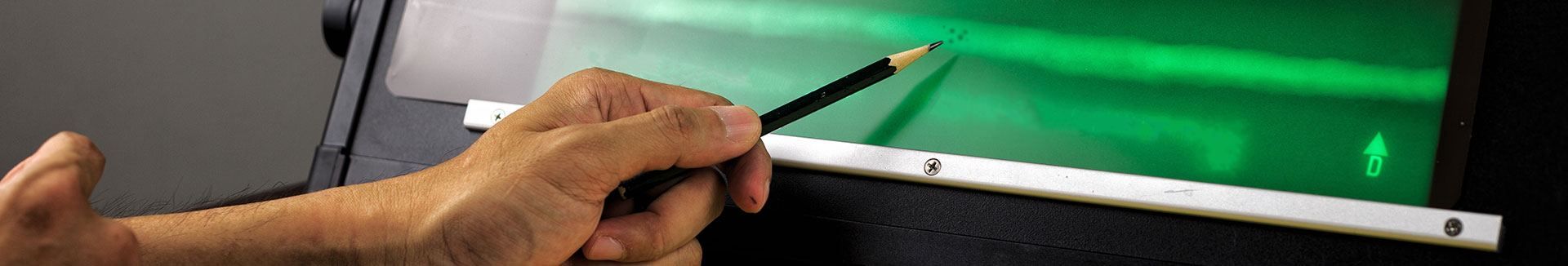 Eine Person hält einen Bleistift vor einem grünen Bildschirm.