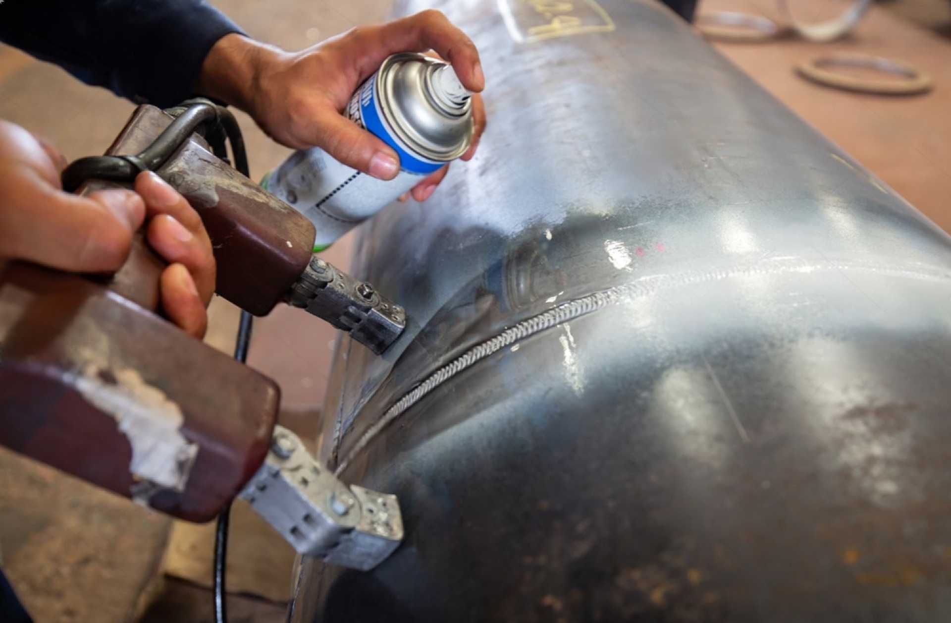 Eine Person sprüht aus einer Spraydose auf ein Metallrohr.