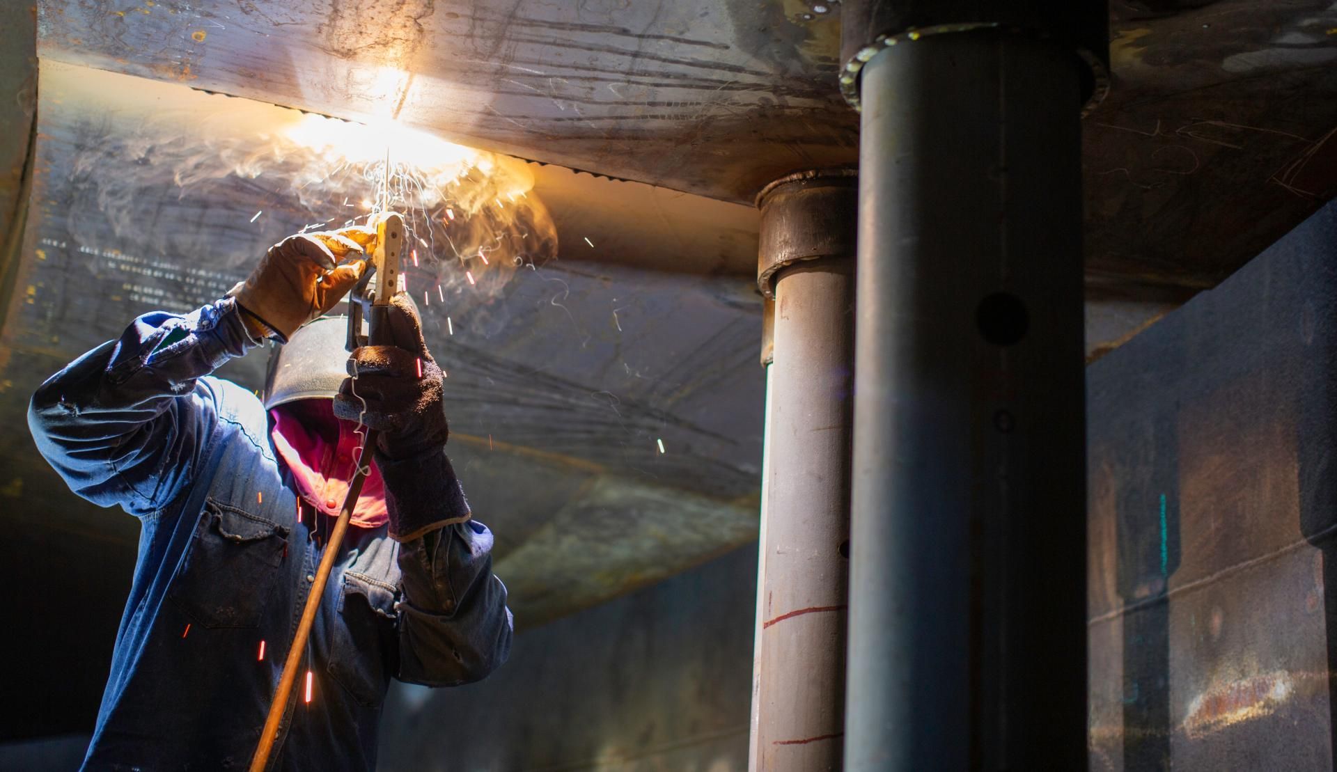 Ein Mann schweißt in einem dunklen Raum ein Rohr.